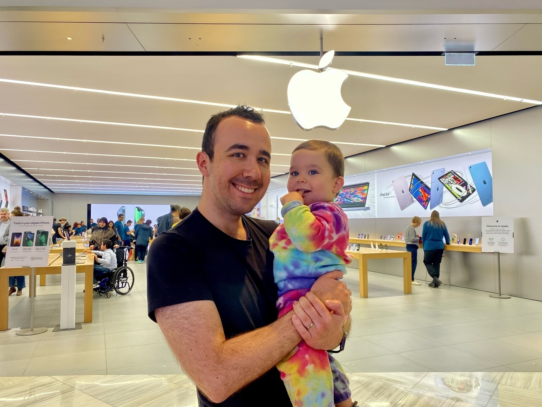 Martin holds Mac while standing in front of an Apple Store, with the company logo and display tables visible in the background