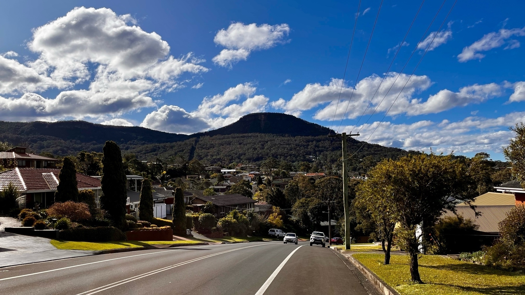 A road going down a hill, with a mountain and blue sky overhead