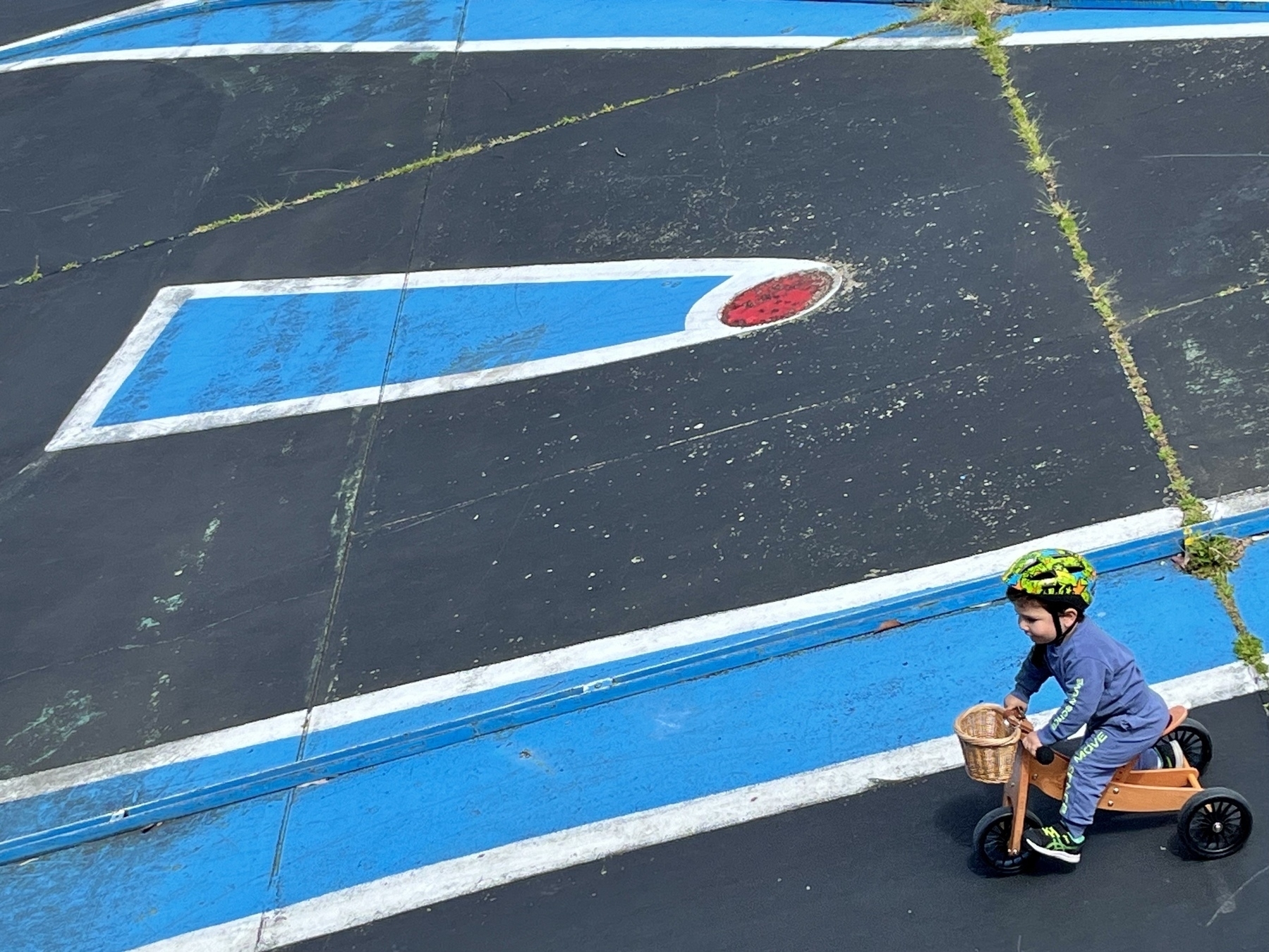 A toddler rides a tricycle on a track for remote-control cars.
