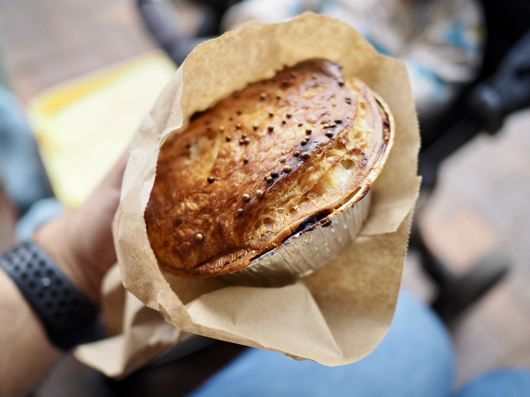 A pie with beautifully-browned pastry, served in a foil tray within a paper bag