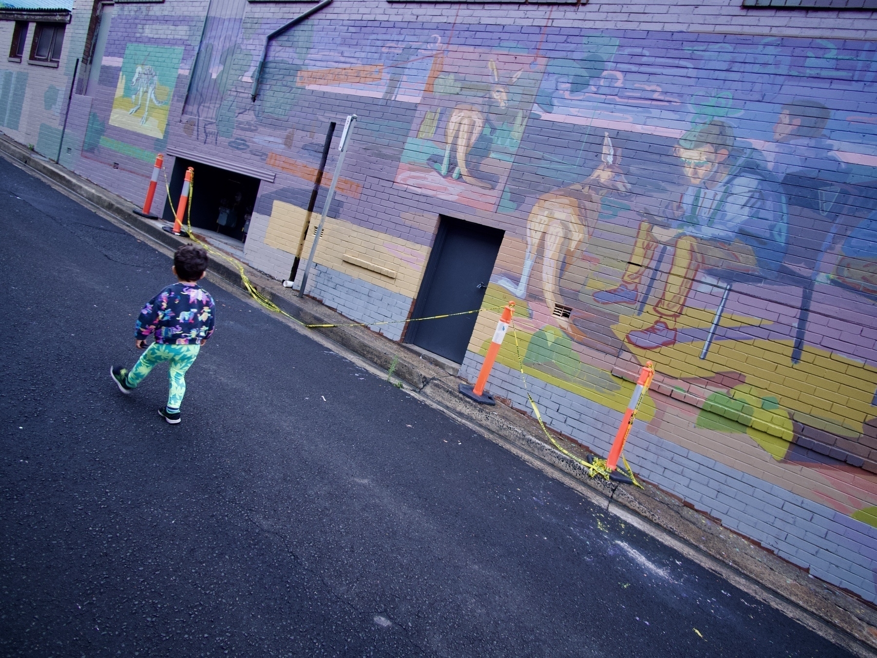 A toddler walks past a mural that features kangaroos.