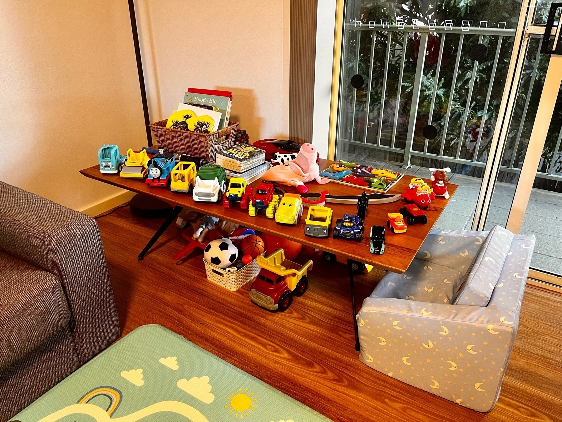 A kid's toys, books and mini-lounge on and around a coffee table, overlooking a balcony and trees