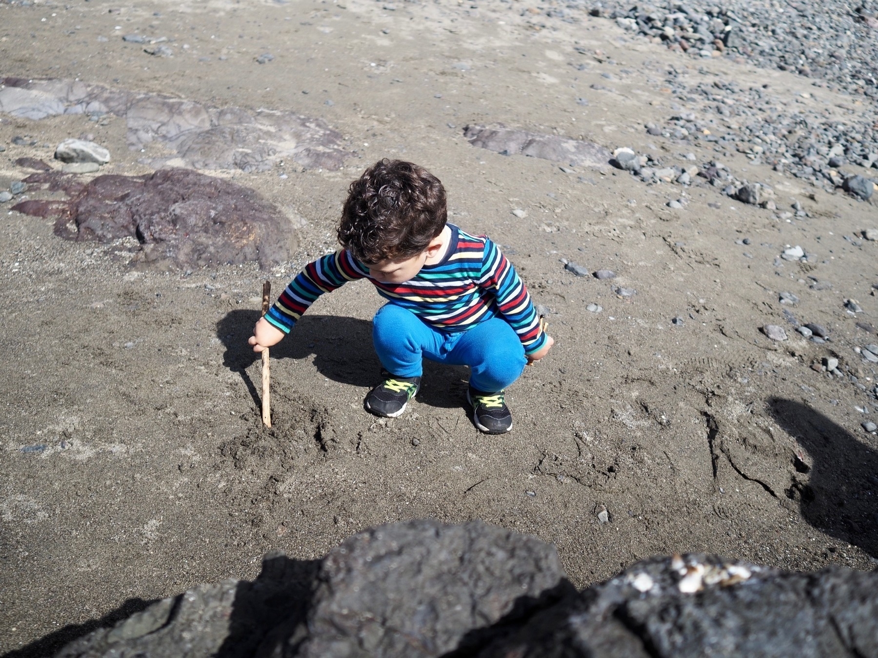 A young boy draws in sand with a stick.