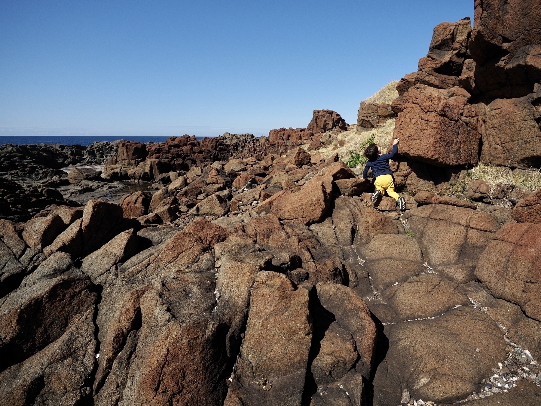 A toddler explores a rocky hill by the sea.