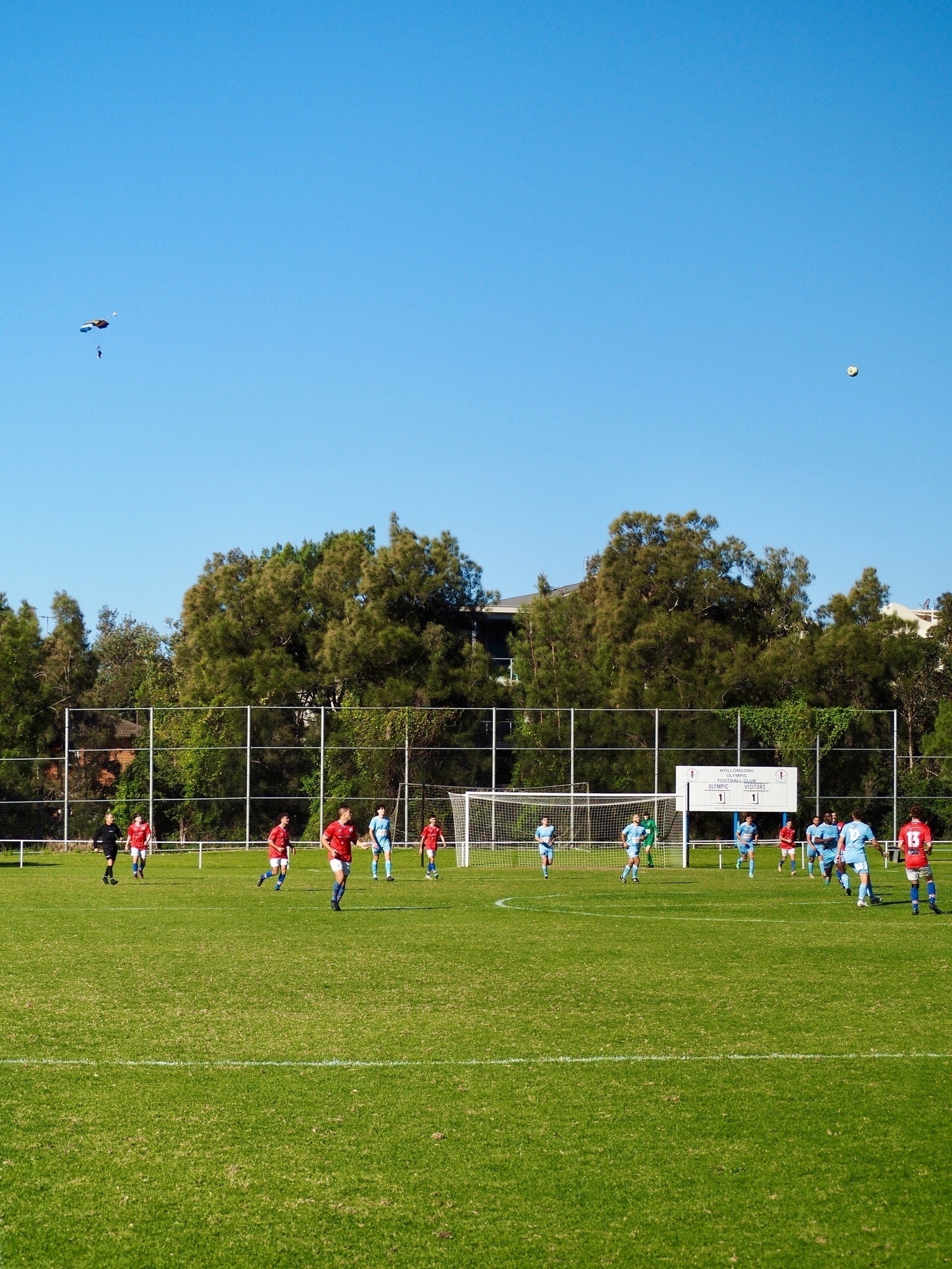 A football match with the ball in the air and a parachute in the sky