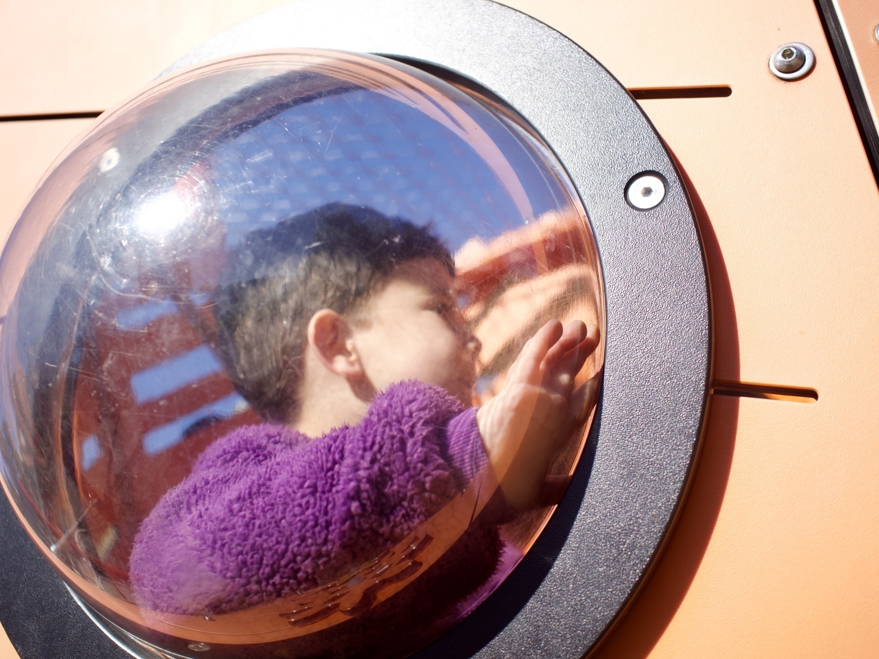 Looking through a blurry circular window at a boy on play equipment