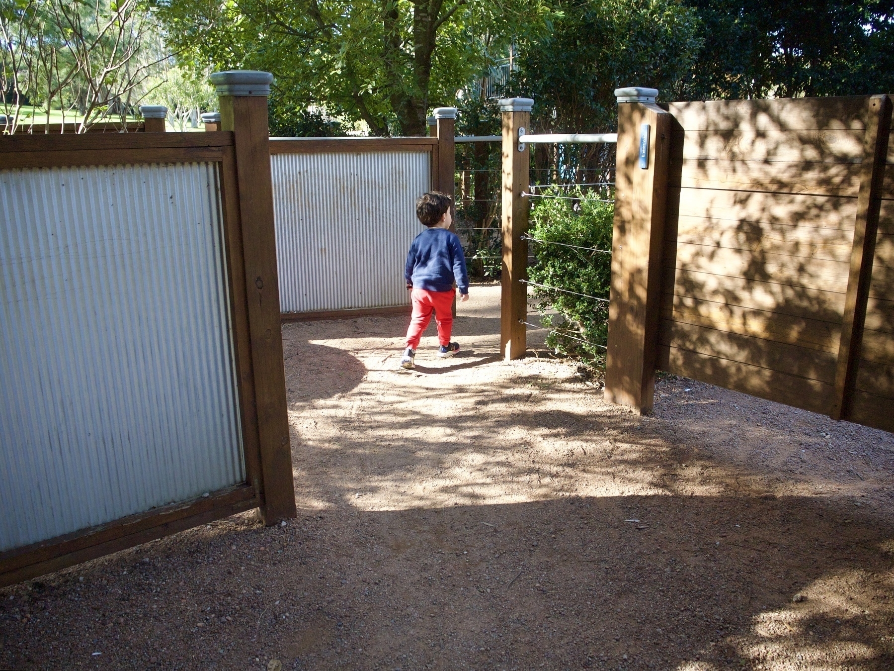 A young boy navigates a garden maze with fences made of wood and steel