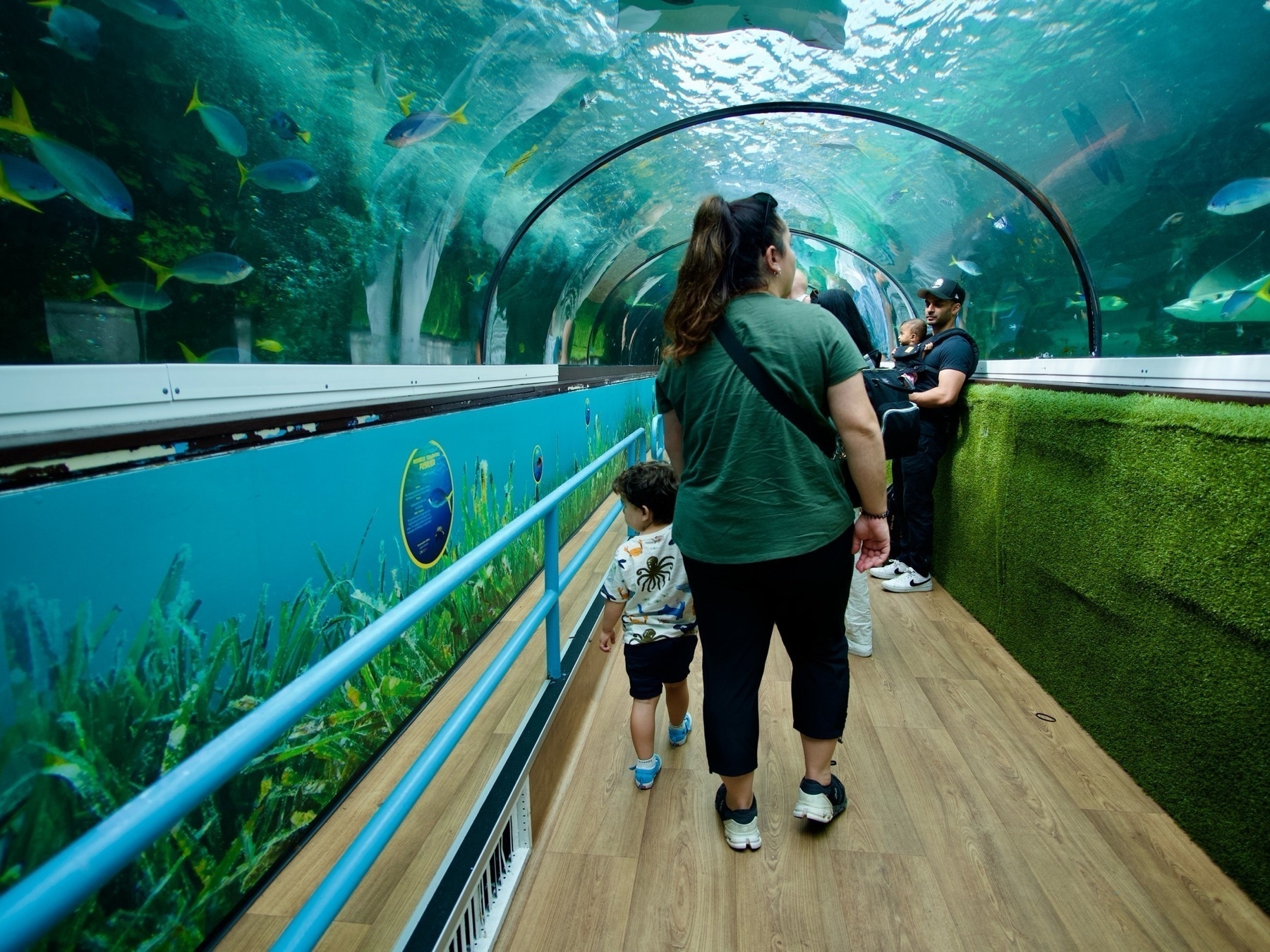 A mother and son walking through a tunnel surrounded by water.