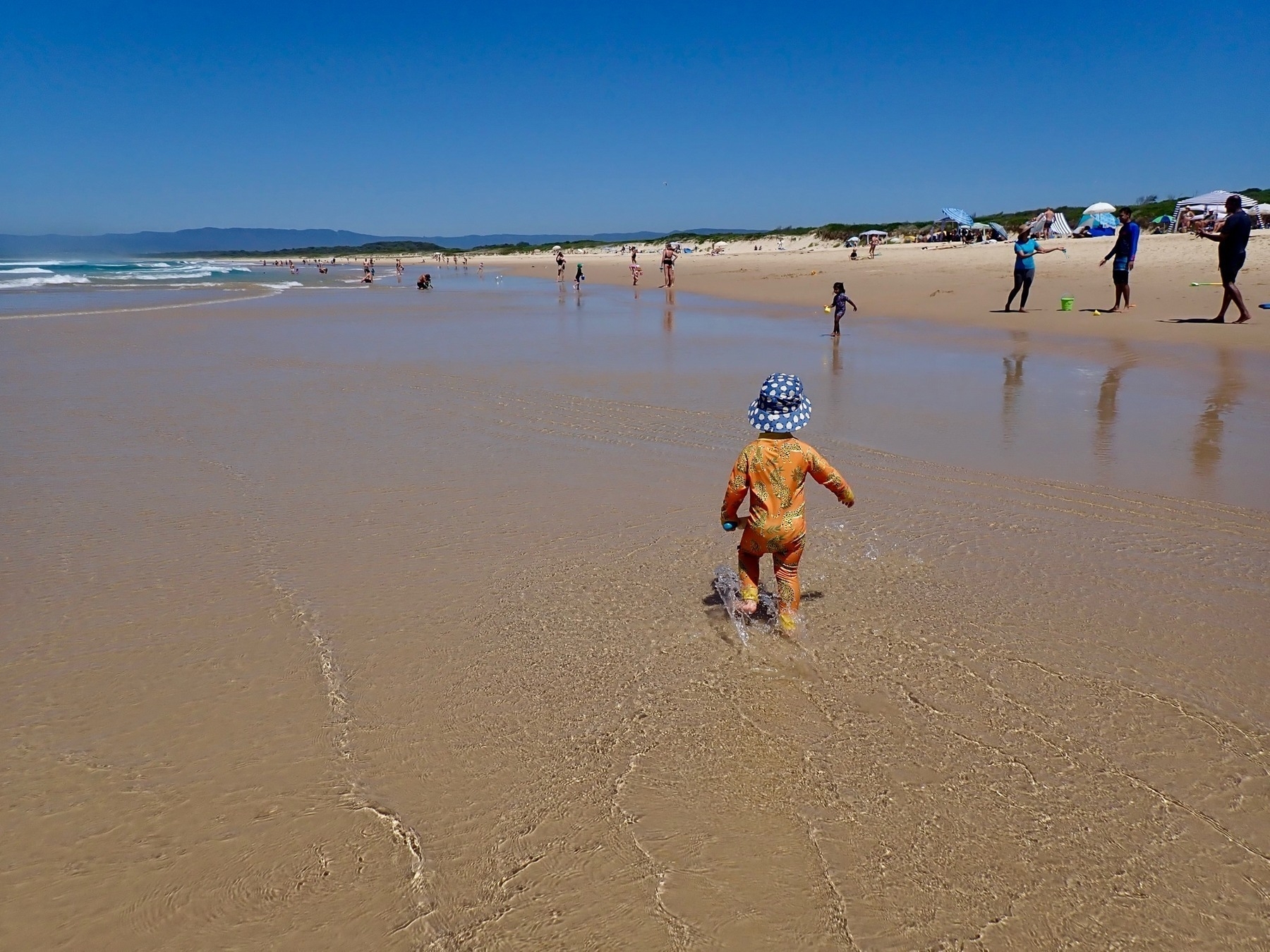 A toddler walks through a low tide.