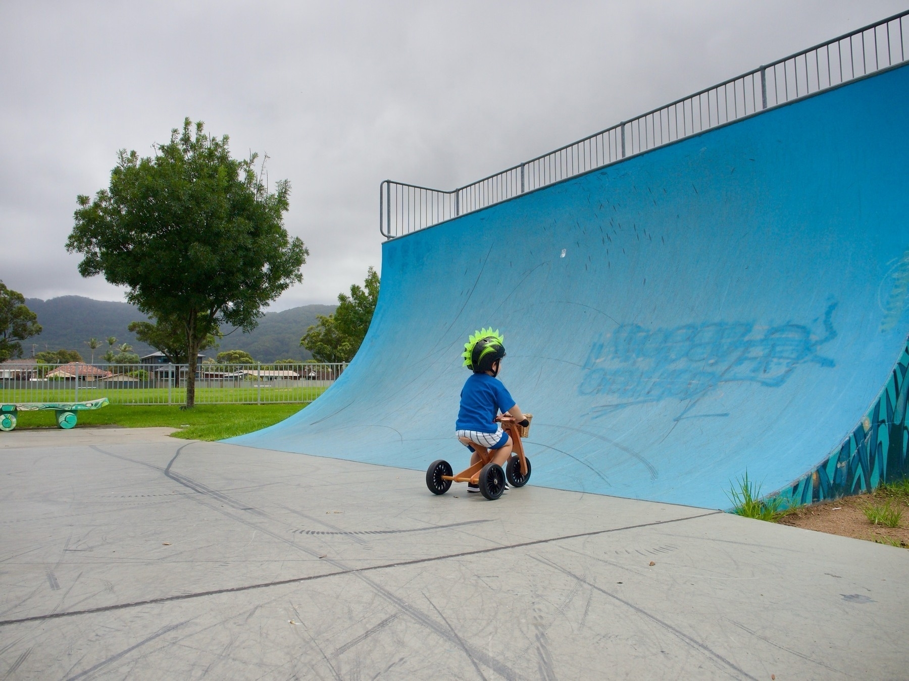 A young boy rides a trike into a half pipe.