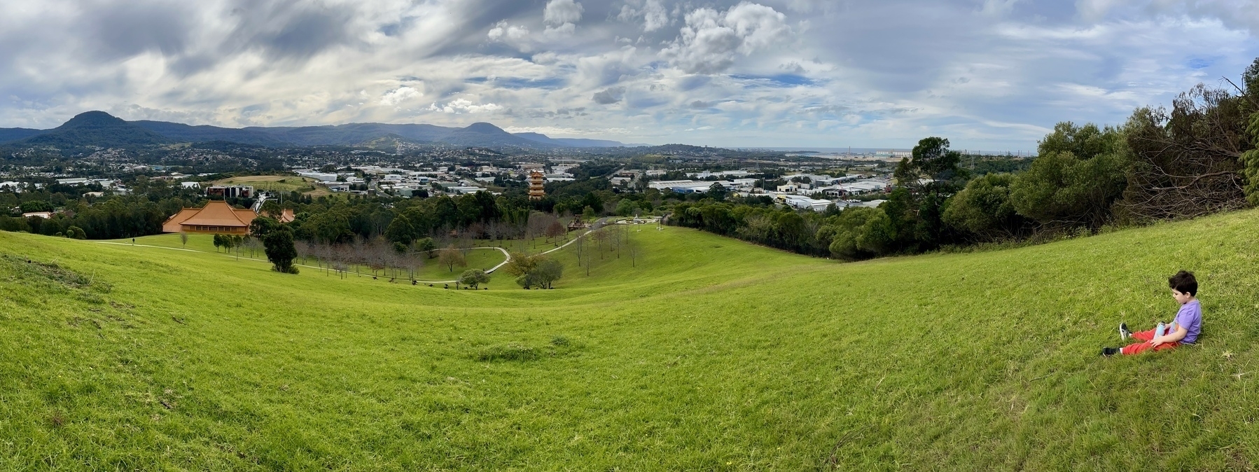 A panorama of rolling hills, a city and a boy in the bottom-right corner