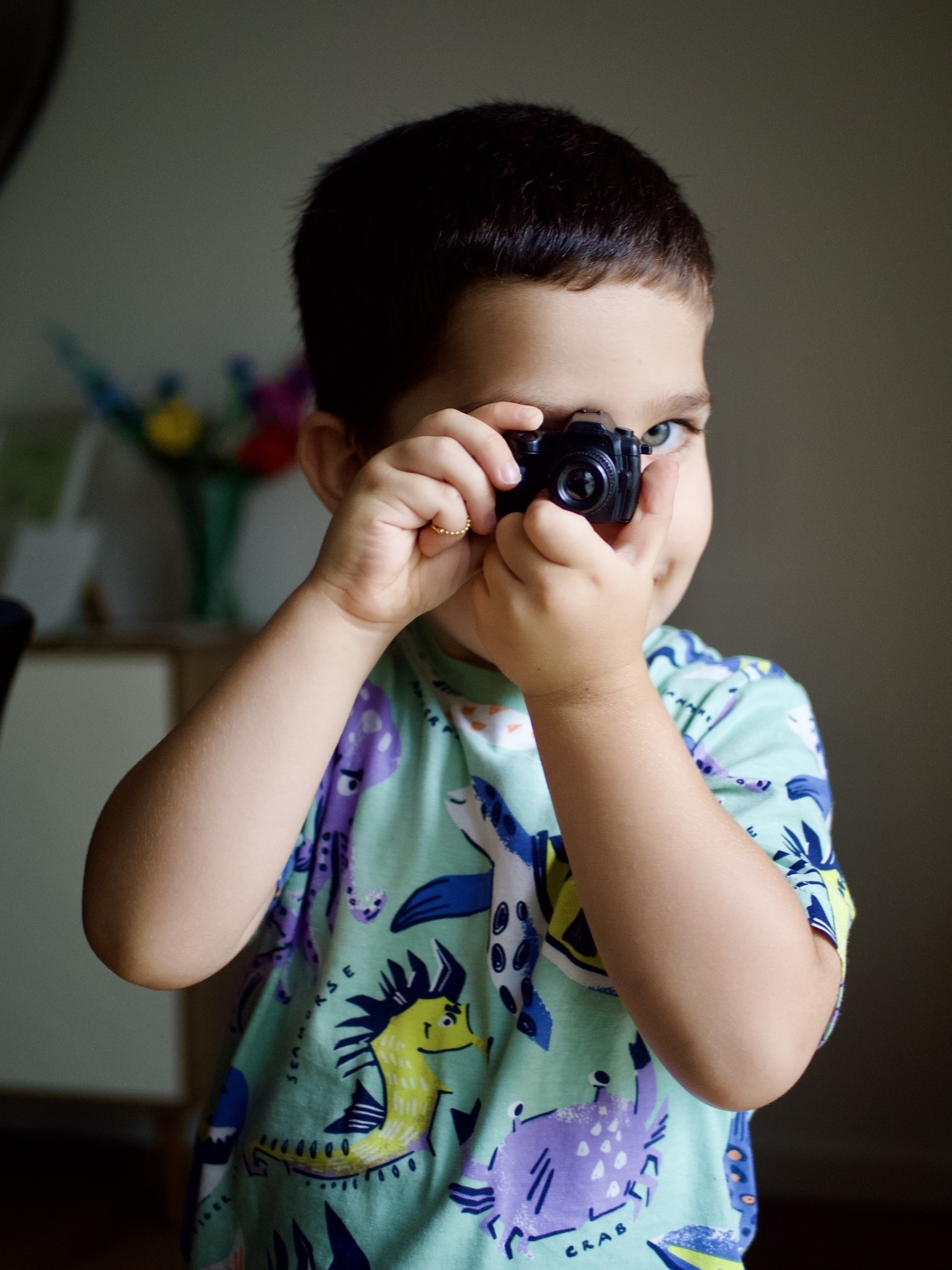 A young boy holds a toy camera up to his right eye.