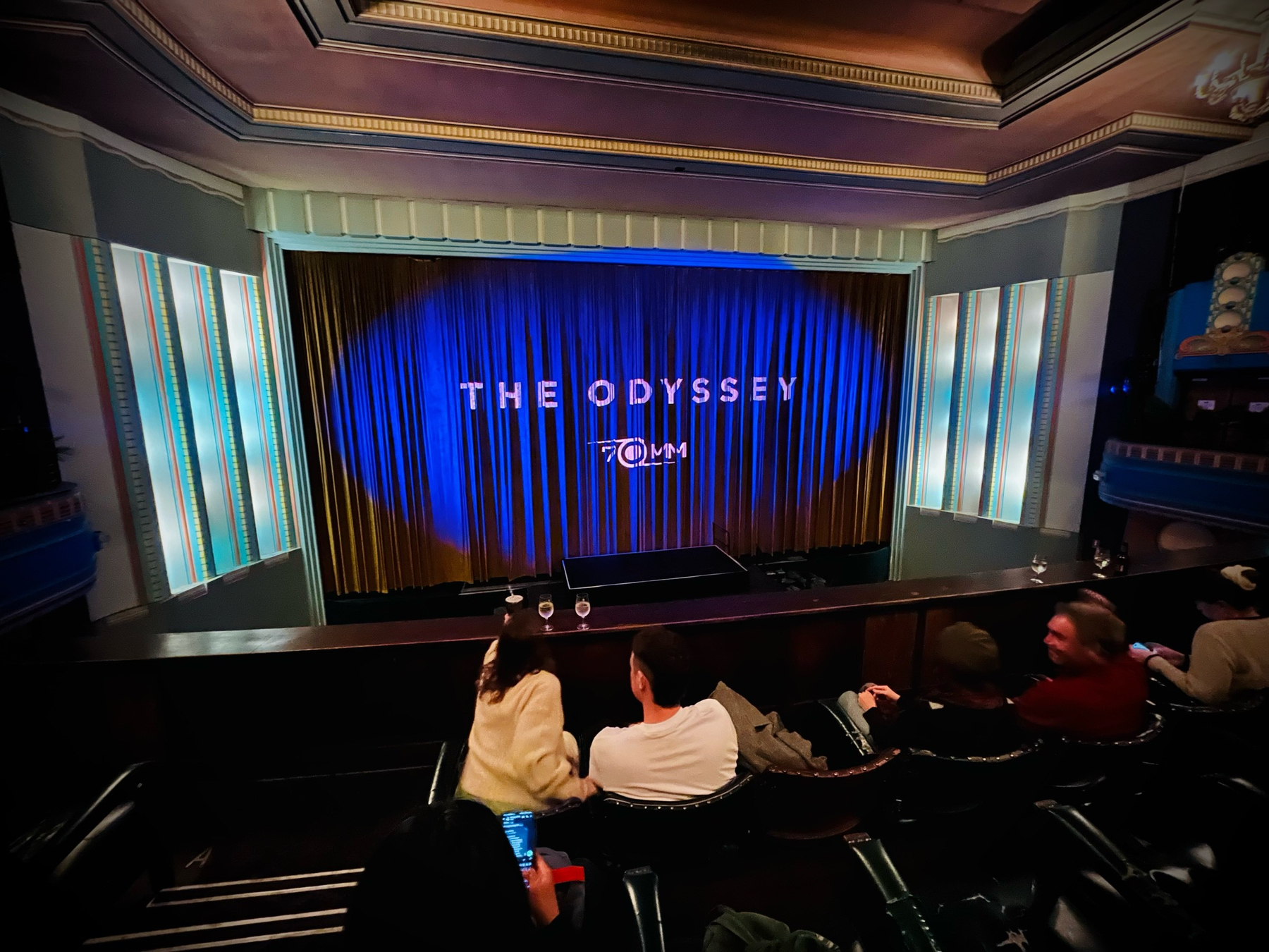 Inside the cinema, looking towards the curtains with the words 'The Odyssey 70mm' projected onto them