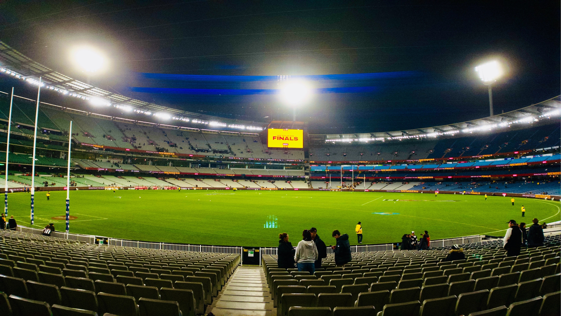 Anamorphic shot of the MCG emptying out, looking over the field towards lights that send streaks of blue flare through the lens