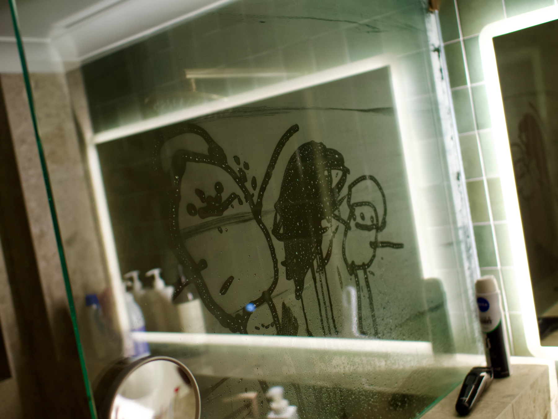 Two bubble people, drawn with a finger on steamy glass, all framed by the reflective light of a bathroom mirror